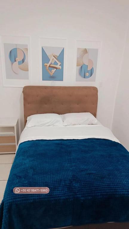 a bed with a blue blanket and pictures on the wall at Apto 5 pessoas - Prox FIP e Stop Shop in Brusque