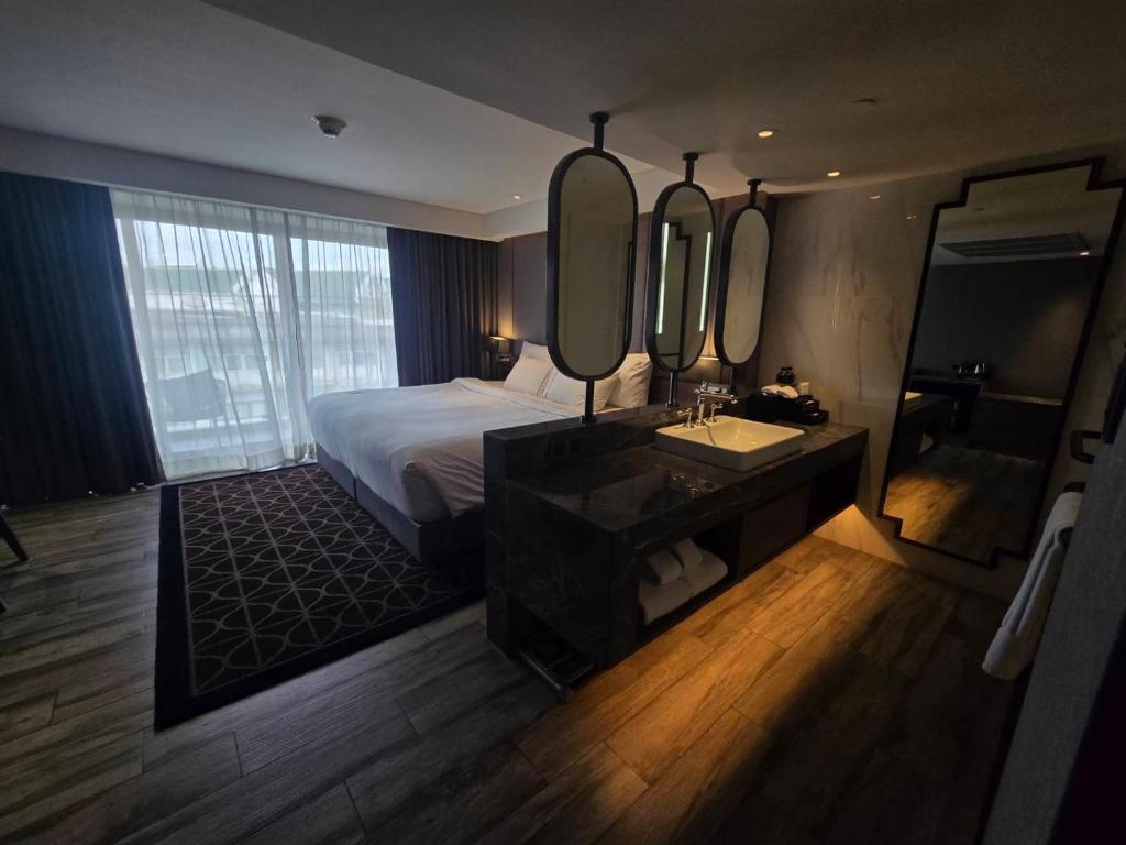 A dark-toned hotel bedroom with a large bed, window wall, and open vanity area.