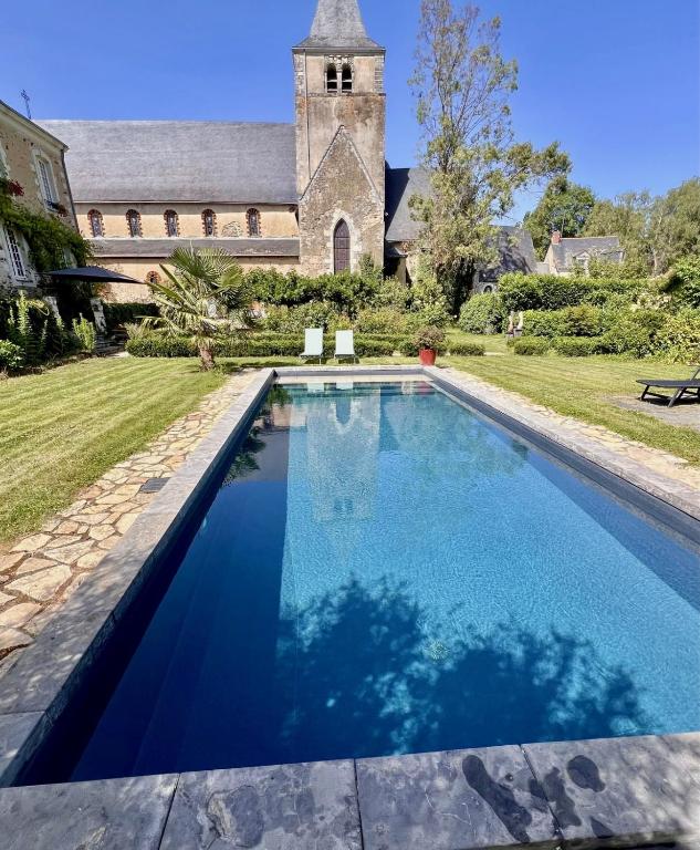 a swimming pool in front of a house with a church at Le Petit Vigneau in Ménil
