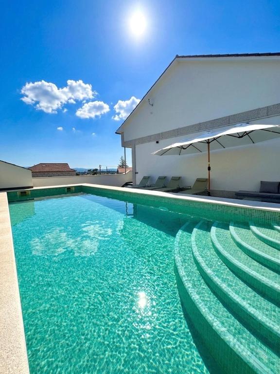 a swimming pool with chairs and an umbrella at Balcón da Ría in Cambados