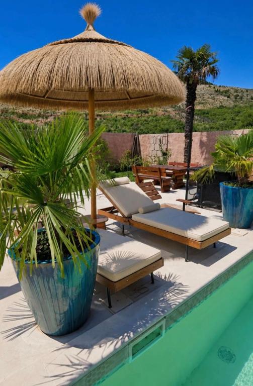 a pool with lounge chairs and a straw umbrella at Villa Aqua Vista in Mostar