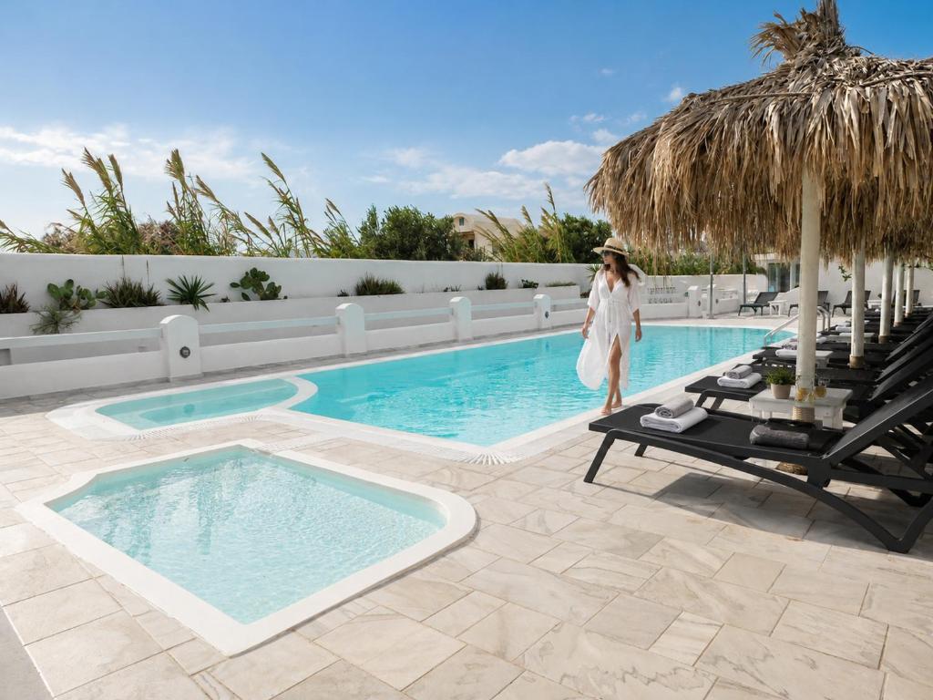 a woman in a white dress is standing next to a swimming pool at Perissa Design Centro Suites- BEACH FRONT in Perissa