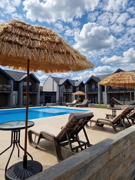 a pool with chairs and a table with a straw umbrella at Apartamenty Marinera in Łeba