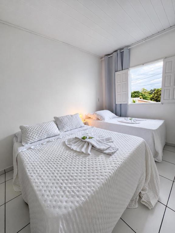 two beds in a white room with a window at Casa Dona Vera - Seu Refúgio no Centro Histórico in Mucugê