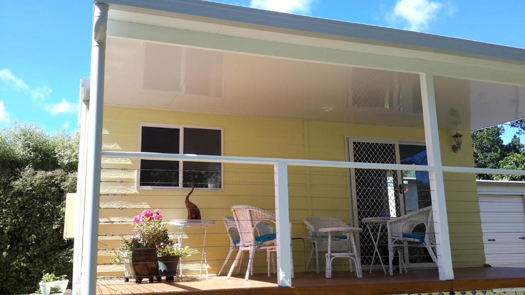 una veranda schermata con sedie e tavoli su una casa gialla di The Best Exotic Magnolia Cottage a Bundanoon