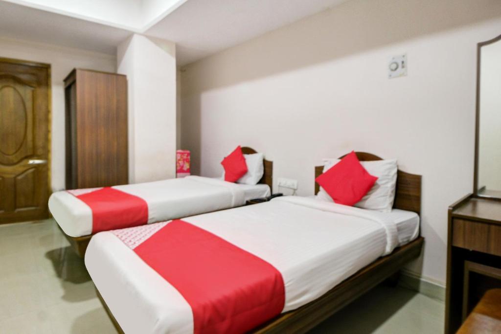 two beds in a hotel room with red and white sheets at Hotel O Ksp Lodge in Neyveli