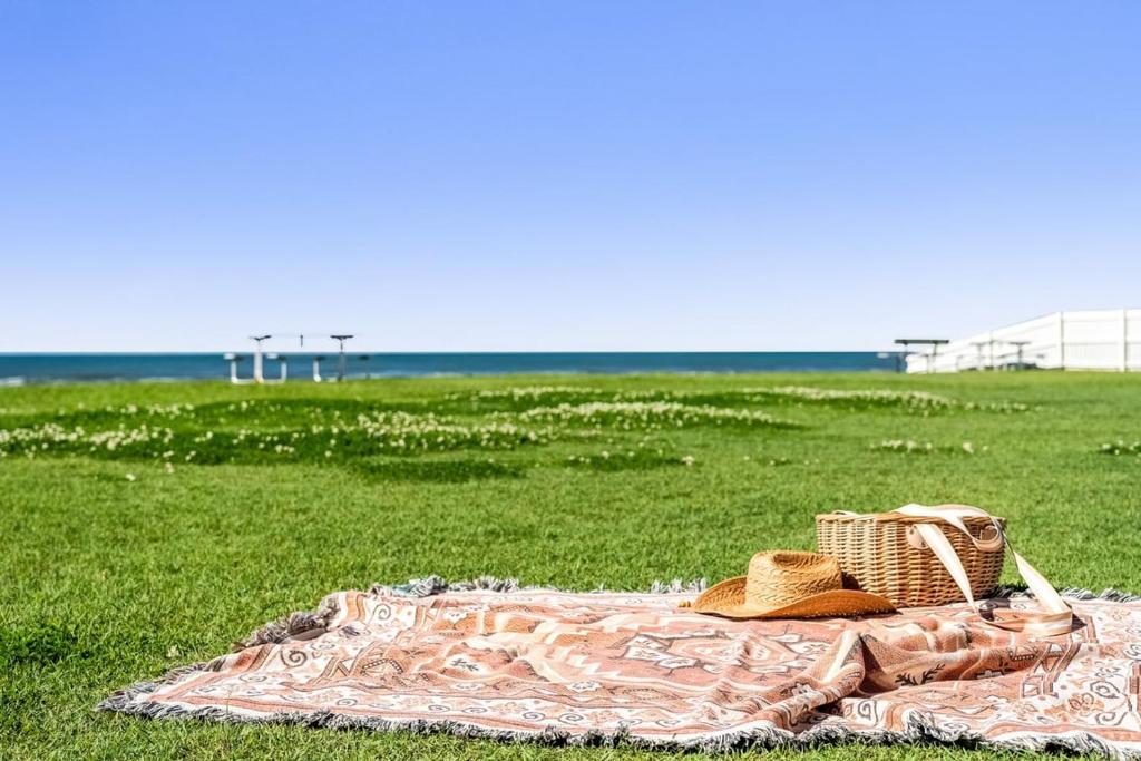 a blanket with hats and a basket on a field at Absolute Beachfront Apartment 2B in Lennox Head