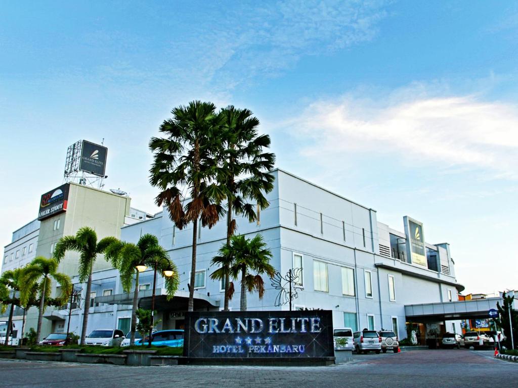 un gran edificio blanco con palmeras delante en Grand Elite Hotel Pekanbaru, en Pekanbaru