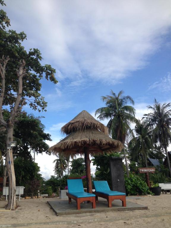 duas cadeiras azuis debaixo de um guarda-sol de palha na praia em Tropicana Khophagan Resort Hotel em Thongsala