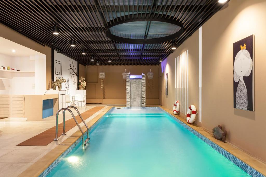 A long indoor pool with a waterfall feature, ladder and adjacent light-colored seating area.
