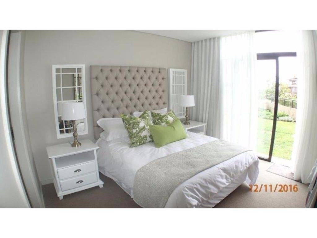 a white bedroom with a large bed with green pillows at Zimbali Suite 104 in Ballito