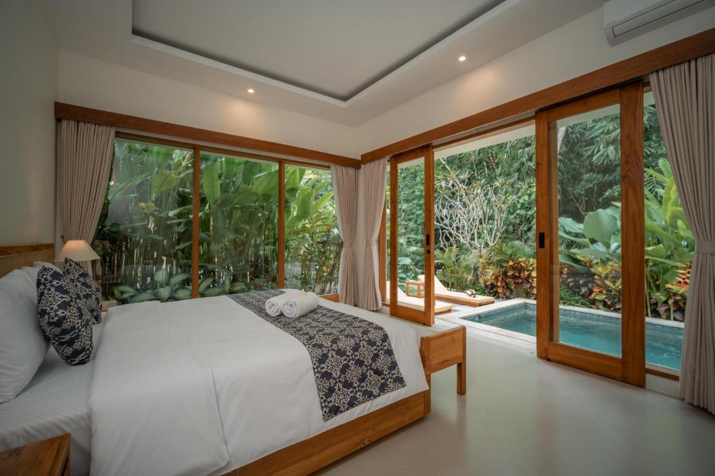 a bedroom with a bed and large windows at River Temple Villa in Ubud