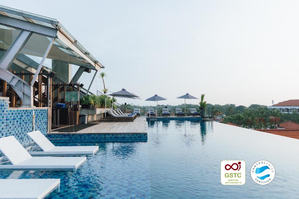 a swimming pool with lounge chairs and umbrellas at ARTOTEL Sanur Bali in Sanur