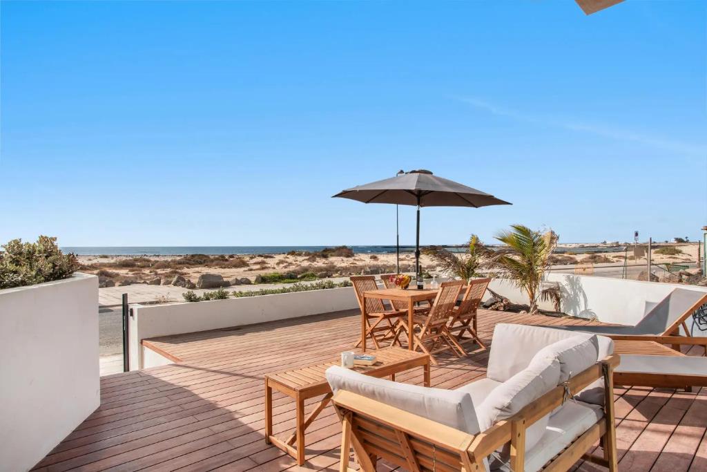 a deck with chairs and an umbrella on the beach at MAAR Suites Cotillo in El Cotillo