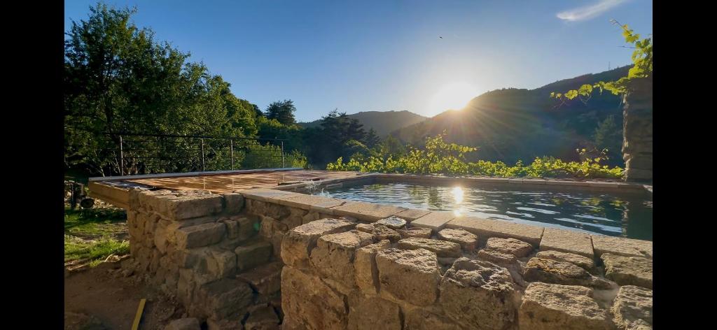 a stone wall around a swimming pool with the sun in the background at La Grange de Bosc -Ardèche verte - Proche train de Lamastre in Saint-Prix