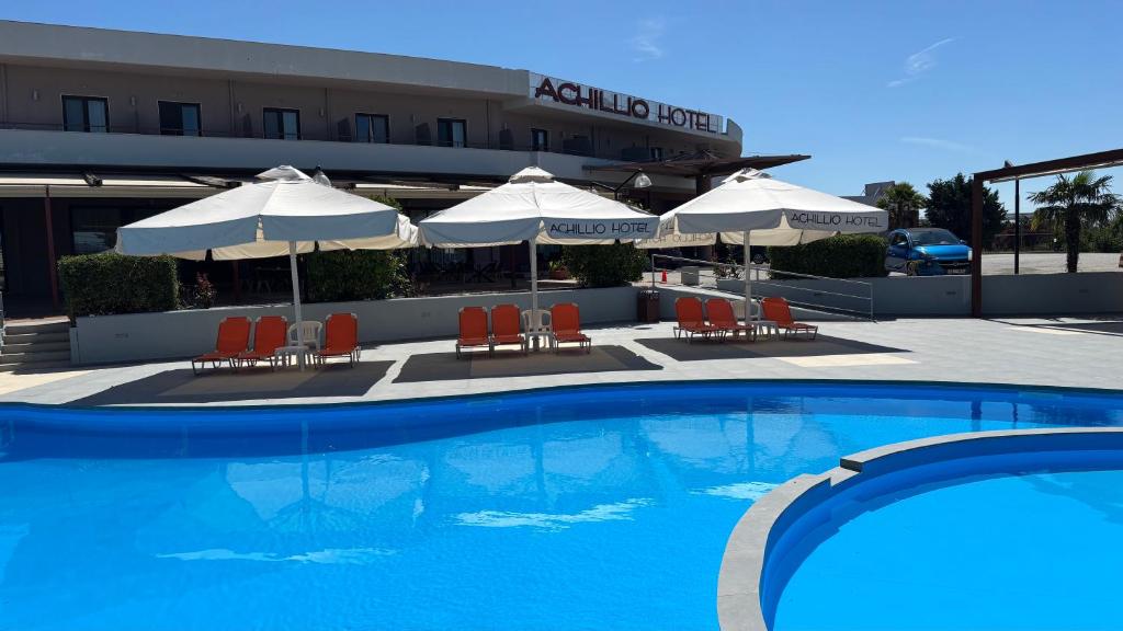 a swimming pool with chairs and umbrellas in front of a hotel at Achillio Hotel in Komotini