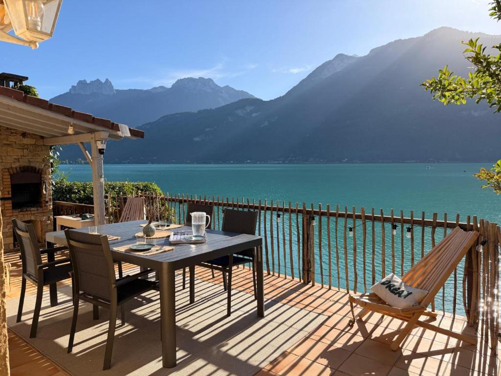 a table and chairs on a deck with a view of a lake at La cabane les pieds dans l'eau, accès direct au lac d'Annecy in Doussard