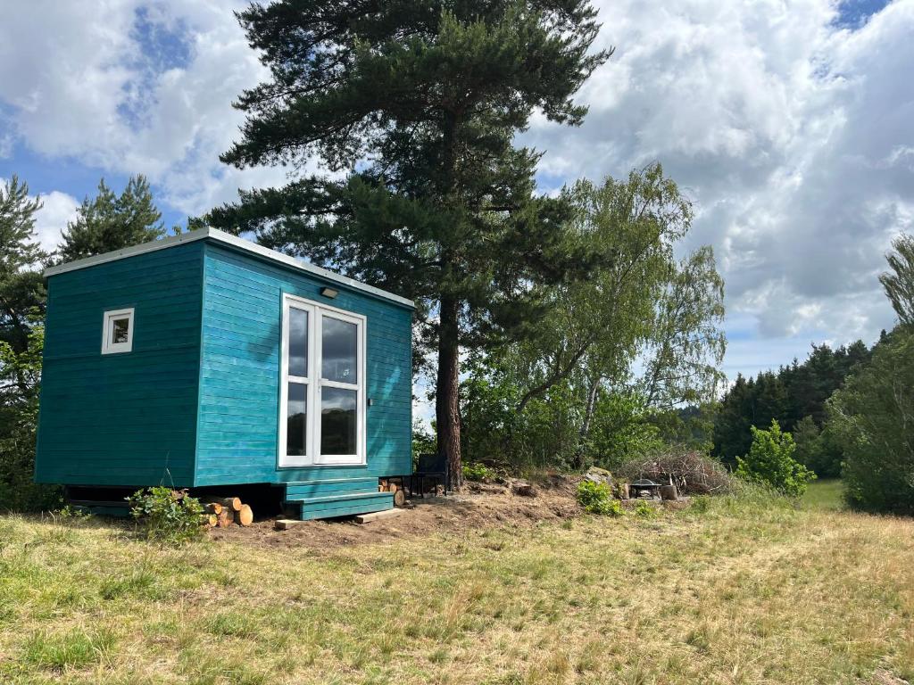 a blue tiny house in a field with a tree at Samoobslužná maringotka in Žihobce