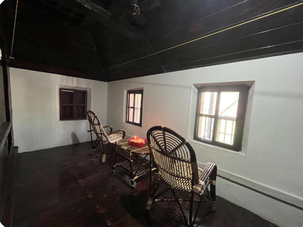 a room with chairs and a table and windows at Heritage Haven in Changanācheri