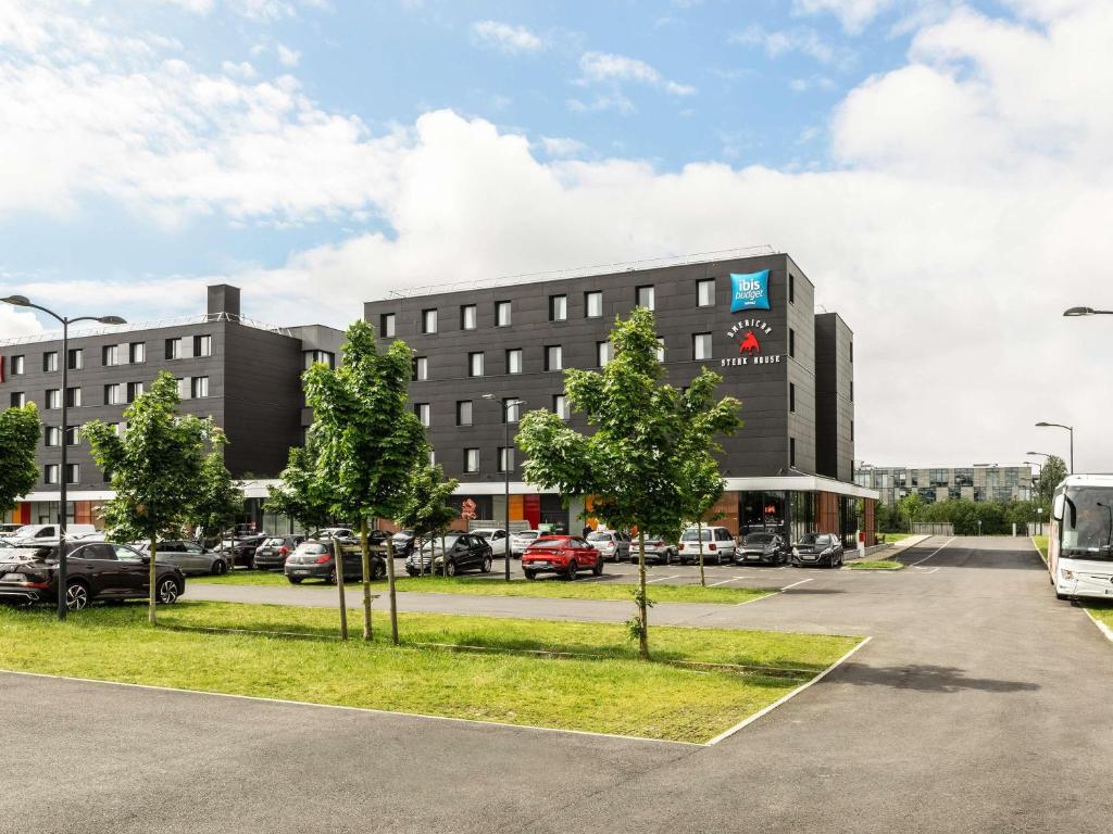 a large building with cars parked in a parking lot at ibis budget Gonesse Le Bourget in Gonesse