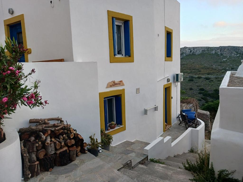a white building with yellow windows and a pile of logs at Levanta Apartment in Kythira