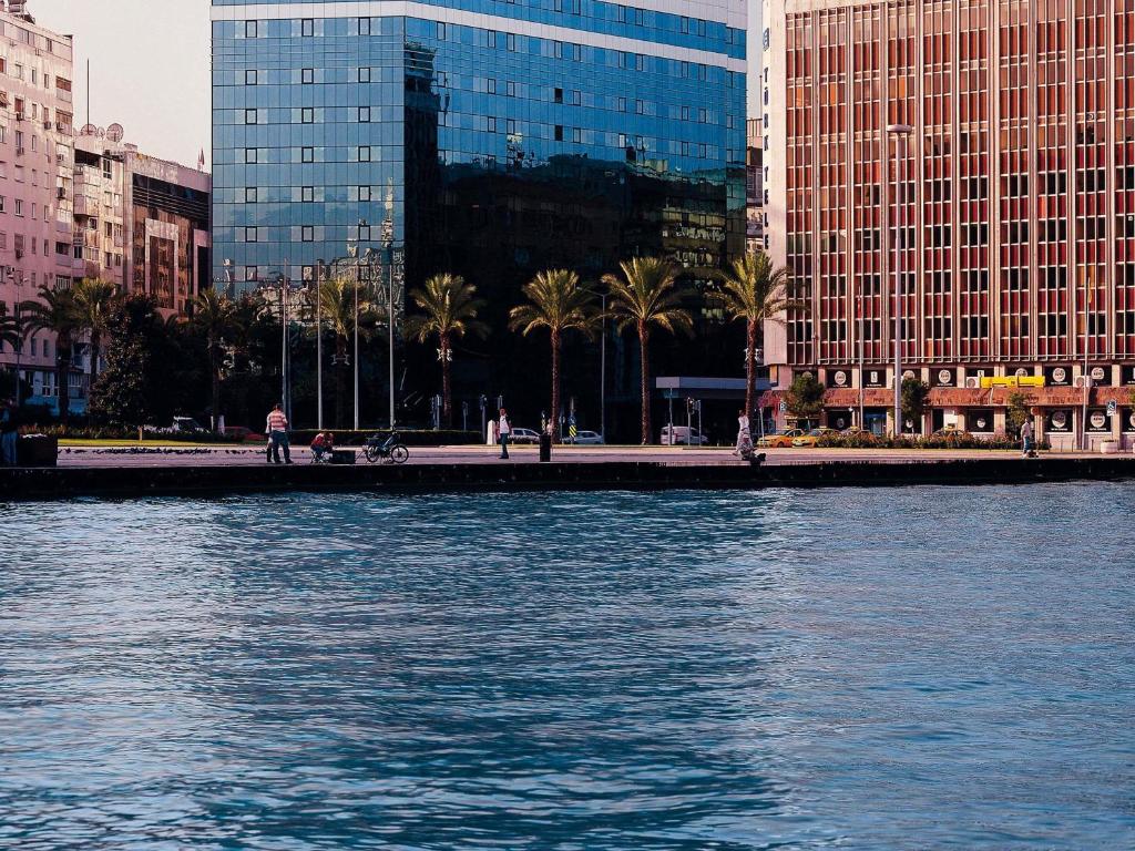 a body of water with buildings and palm trees at Mövenpick Hotel Izmir in İzmir