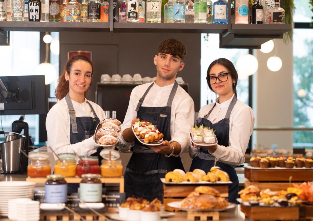 three people standing in a kitchen holding plates of food at Clipper in Pesaro