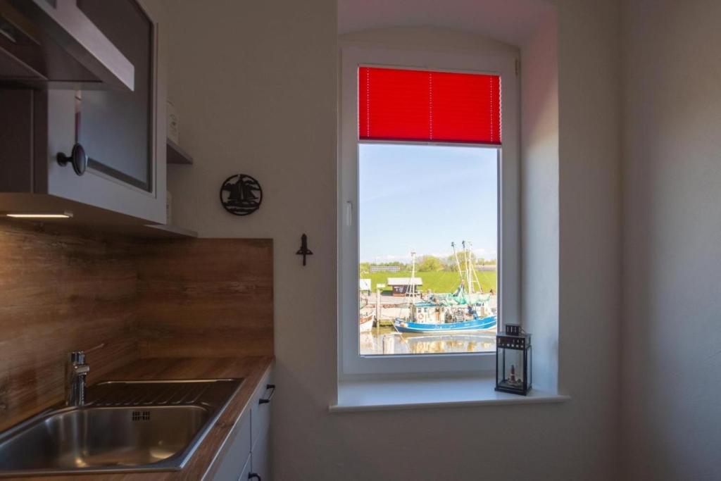 a kitchen with a red window with a view of a marina at Heimathafen über dem Hafen - Pub in Pellworm