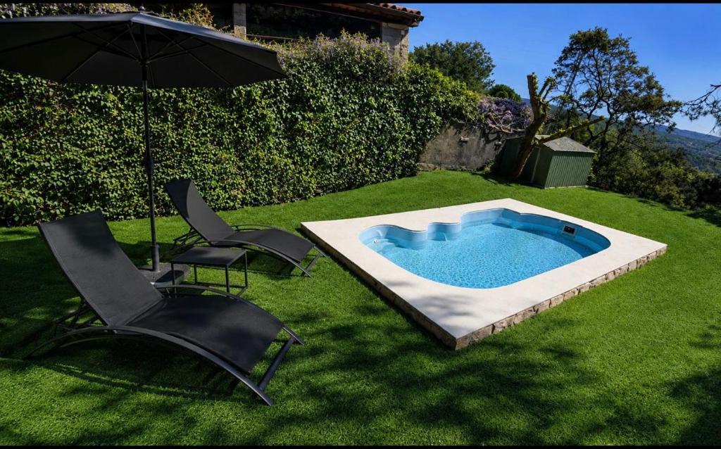 a swimming pool in the grass with two chairs and an umbrella at Alojamientos del Valle in Sotillo de la Adrada