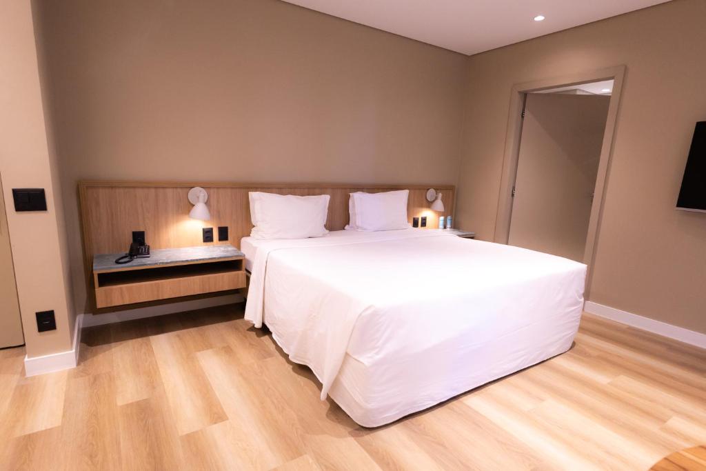 a bedroom with a large white bed and wooden floors at Intercity Faria Lima Address in São Paulo
