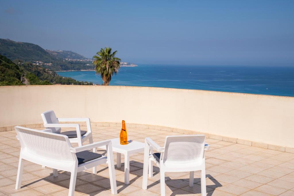 a table with white chairs and a bottle of wine at Villa Chiara Infinity Sea View in Mandaradoni