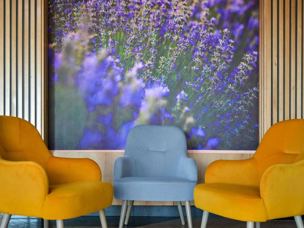 three chairs in front of a painting of purple flowers at Mercure Medias Binderbubi Hotel And Spa in Mediaş