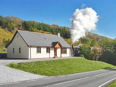 a white house with a steam train in the distance at Blythswood in Glenfinnan