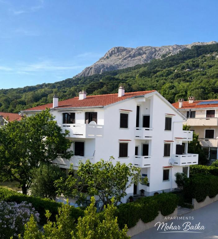 a white building with a mountain in the background at Apartments Mohar III in Baška