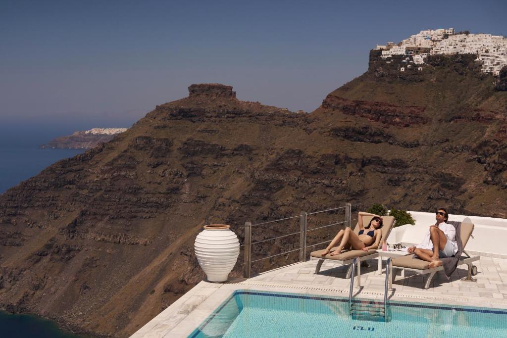 two people sitting in chairs next to a swimming pool at Homeric Poems in Fira