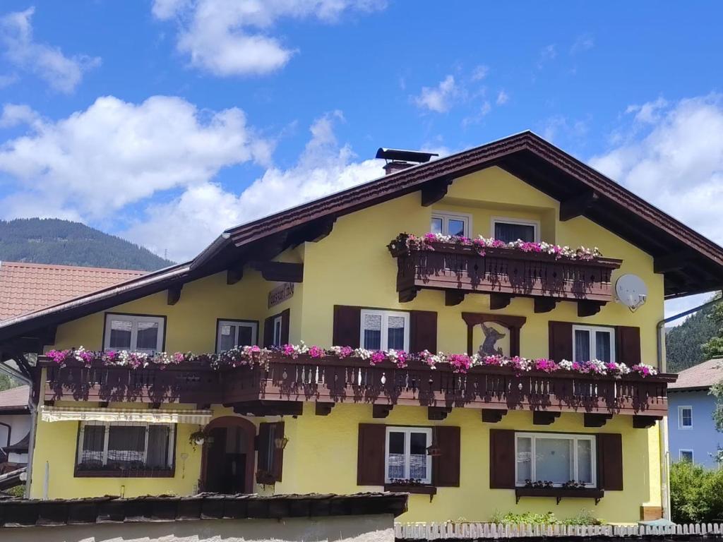 a yellow house with a balcony with flowers at Haus zur Linde in Wagrain