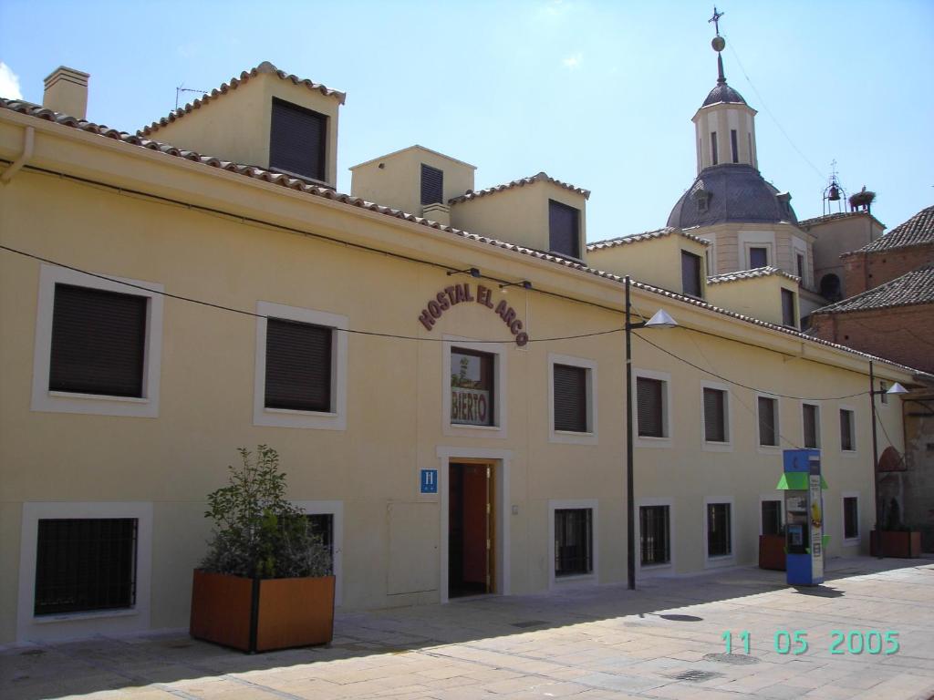 un grand bâtiment jaune avec une église en arrière-plan dans l'établissement Hostal El Arco, à Mejorada del Campo