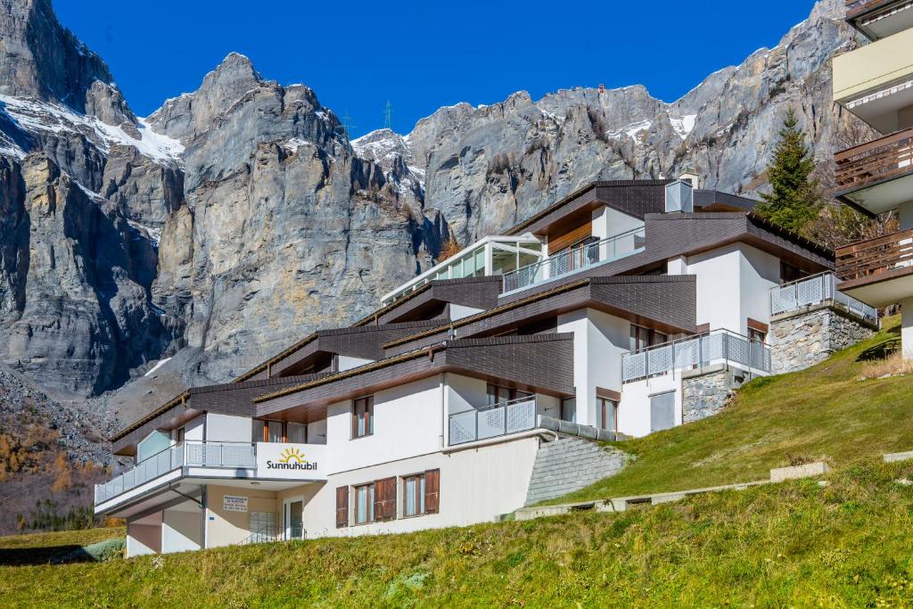 ein Gebäude auf einem Hügel mit Bergen im Hintergrund in der Unterkunft Sunnuhubil Leukerbad in Leukerbad