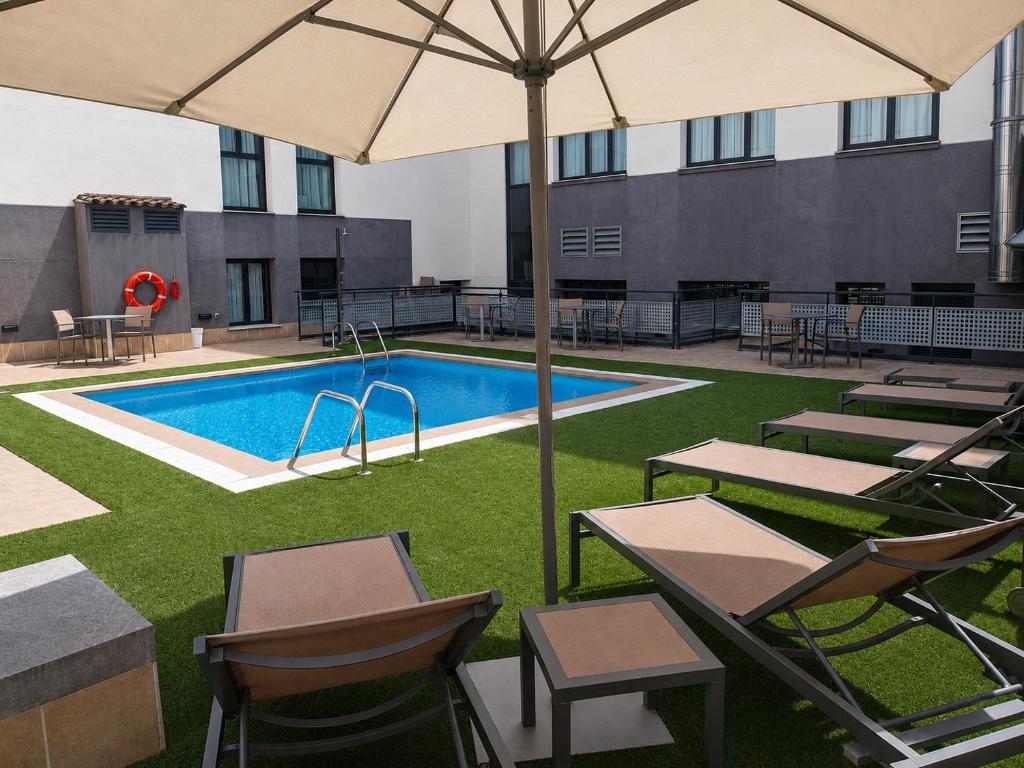 a pool with tables and chairs and an umbrella at Hotel Pedro I de Aragón 4 Sup in Huesca