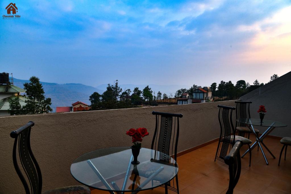 a table and chairs on a balcony with a view at CHOCOLATE VILLA Mahabaleshwar in Mahabaleshwar