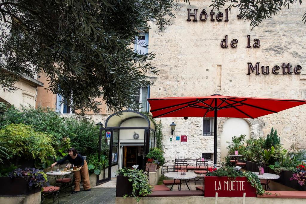 a man sitting in front of a hotel with a red umbrella at Hôtel La Muette in Arles