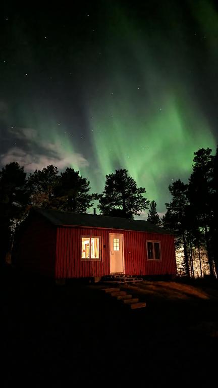 a red cabin with the green northern lights in the sky at NorrskensRo in Kiruna
