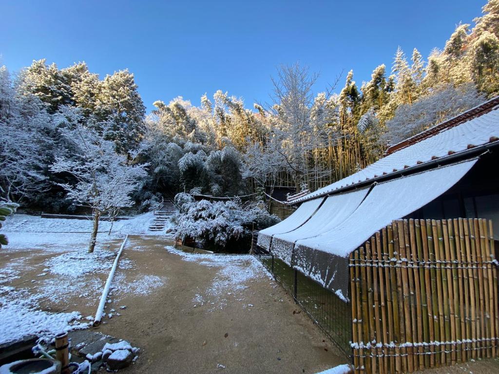 a house covered in snow with a fence and trees at うさぎのキャンプ広場 in Oguni