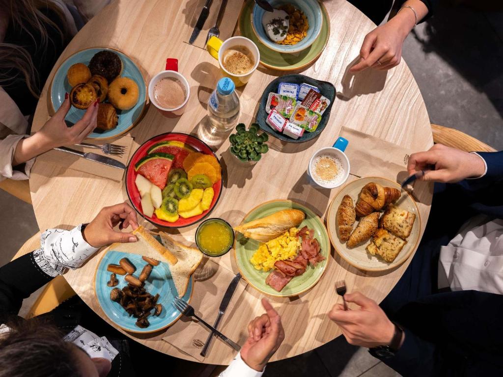 A communal breakfast table covered with pastries, fruit, eggs, bread, drinks and spreads.