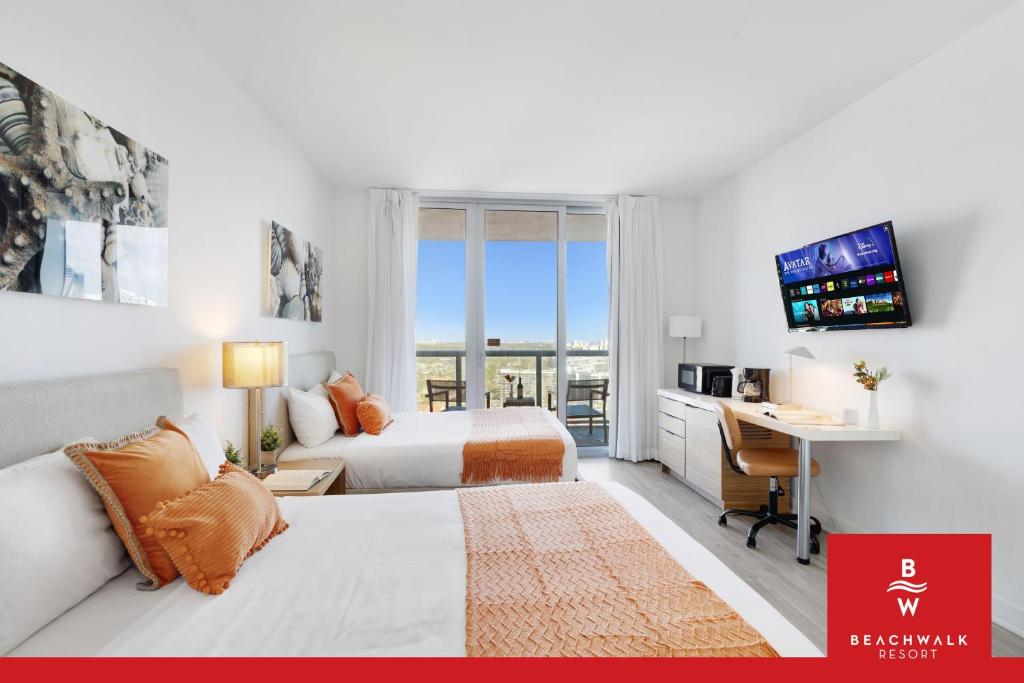 a hotel room with two beds and a desk and a television at Upper-Floor Studio Balcony Sleeps 4 in Hallandale Beach