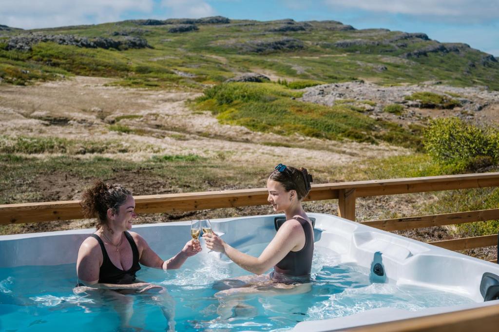 two women sitting in a bath tub with glasses of wine at Hvammur 10 with private hot tub in Kaldrananes