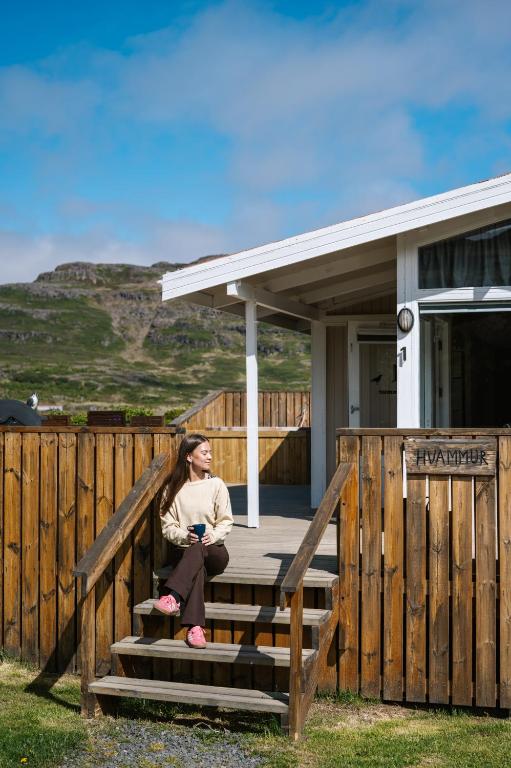 a woman sitting on the stairs of a house at Hvammur 1 with private hot tub in Drangsnes
