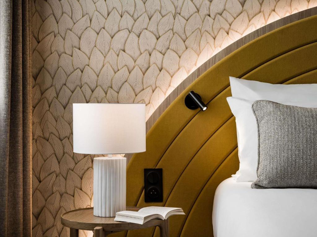 a bed with a lamp on a table with a book at Mercure Chartres Est in Chartres
