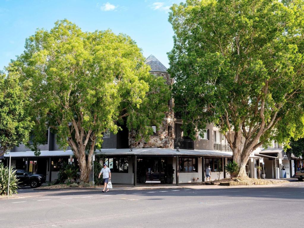 a person walking in front of a building with trees at The Sebel Byron Bay in Byron Bay