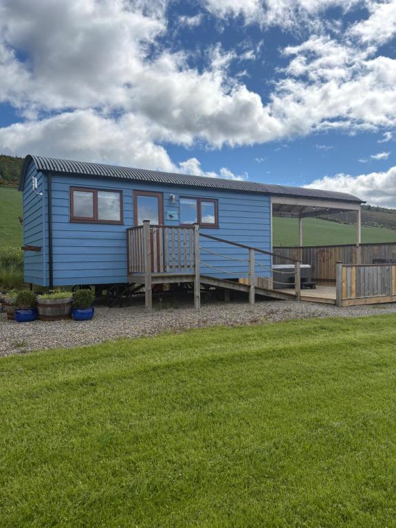 a blue tiny house with a porch and a deck at Ledmacoy Shepherds Huts in Strathdon